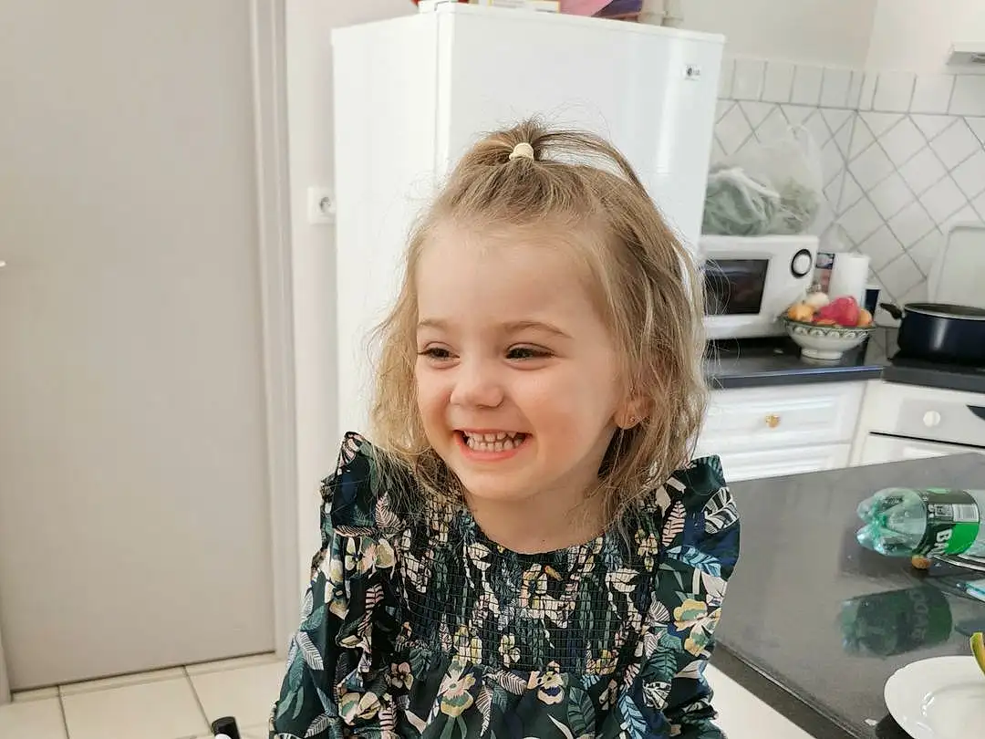 Hair, Sourire, Kitchen Sink, Sink, Tap, Sleeve, Kitchen, Countertop, Kitchen Appliance, Cabinetry, Happy, Bambin, T-shirt, Plumbing Fixture, Cooking, Kitchen Stove, Room, Blond, Enfant, Home Appliance, Personne, Joy