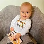 Baby & Toddler Clothing, Sleeve, Comfort, Sourire, Baby, Bambin, T-shirt, Collar, Knee, Sock, Assis, Enfant, Human Leg, Thigh, Pattern, Book, Couch, Happy, Personne