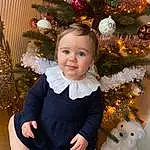 Christmas Tree, Head, Photograph, Yeux, Facial Expression, Blanc, Light, Sourire, Human Body, Sleeve, Happy, Debout, Christmas Ornament, Dress, Iris, Baby & Toddler Clothing, Bambin, Christmas Decoration, Holiday Ornament, Personne, Joy