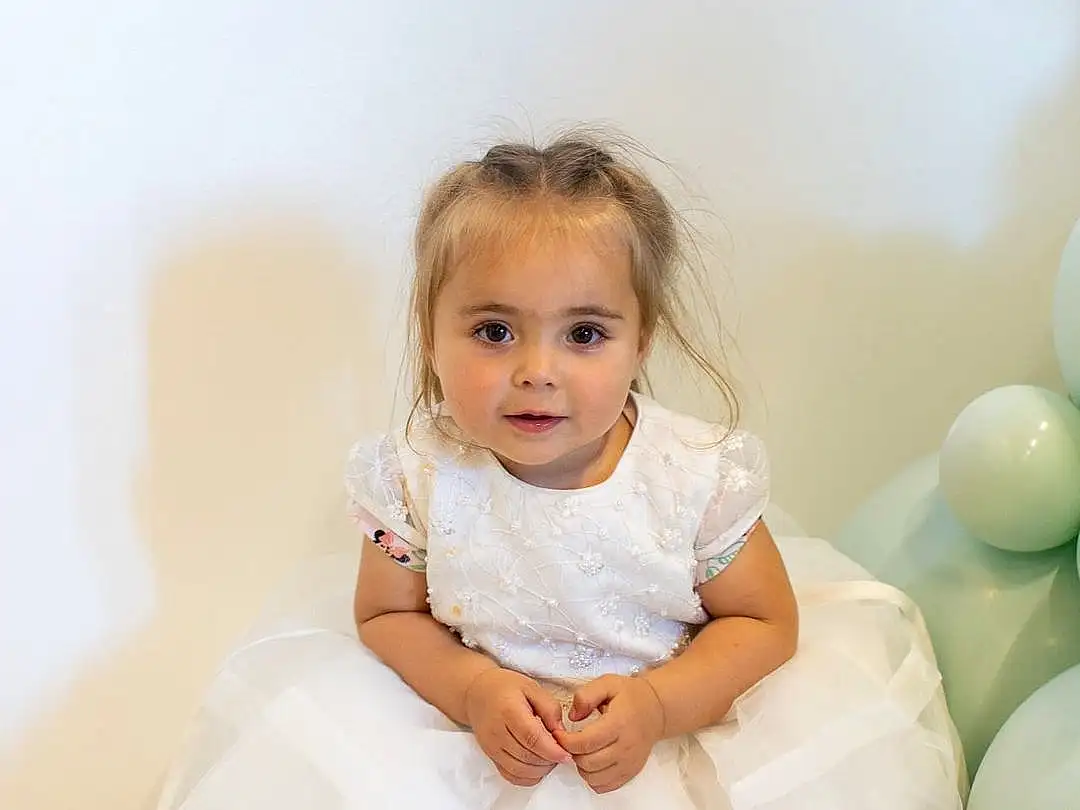 Peau, Dress, Flash Photography, Happy, Gesture, Balloon, Baby & Toddler Clothing, Baby, Bambin, Event, Fun, Blond, Bridal Accessory, Enfant, Assis, Formal Wear, Jewellery, Portrait Photography, Room, Personne